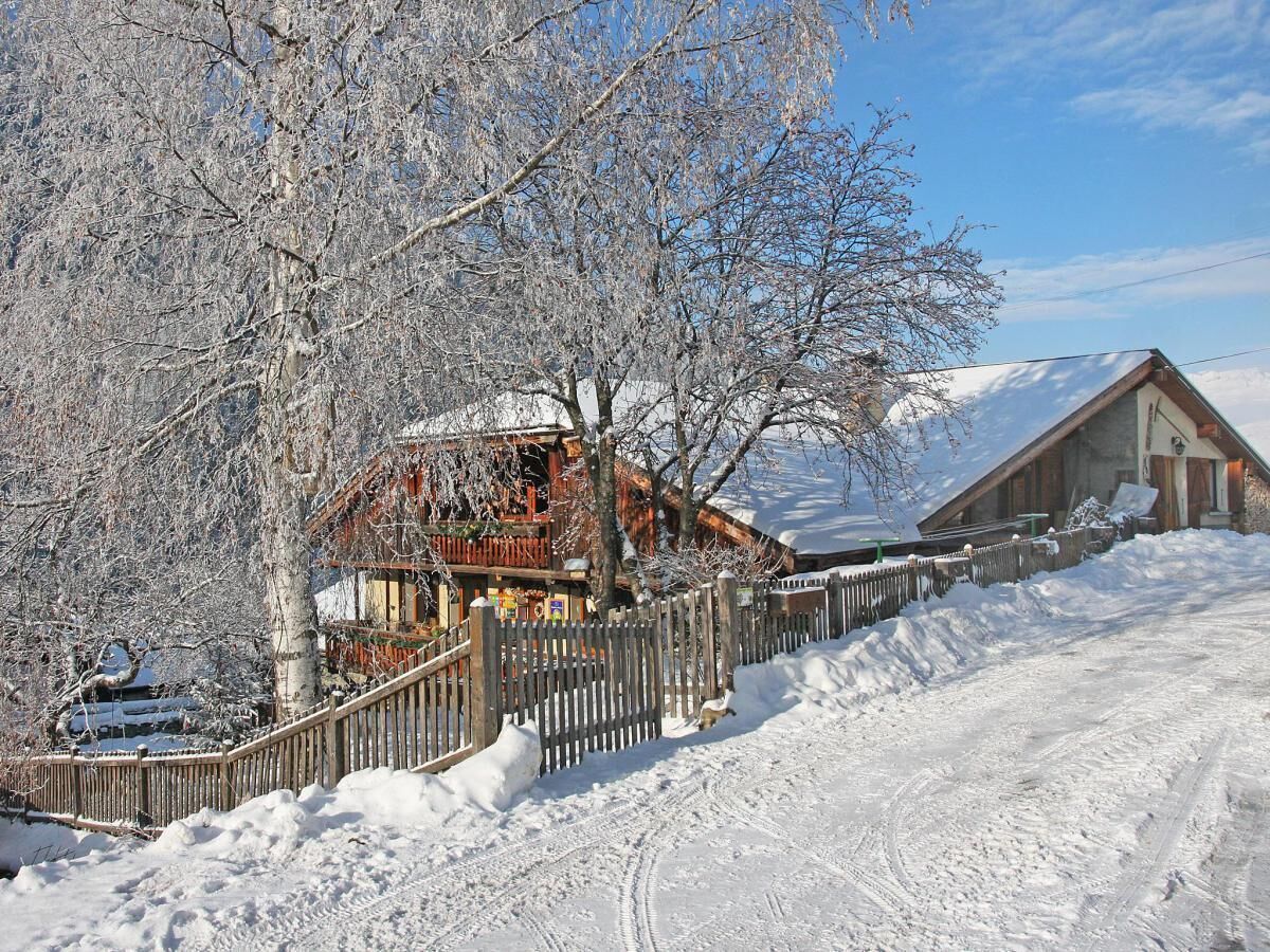 A wooden cabin with a snow-covered roof, surrounded by a wooden fence and a snow-covered path.