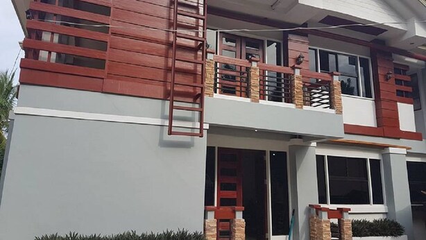 Una casa moderna de dos pisos con un balcón, una escalera visible y una entrada principal.