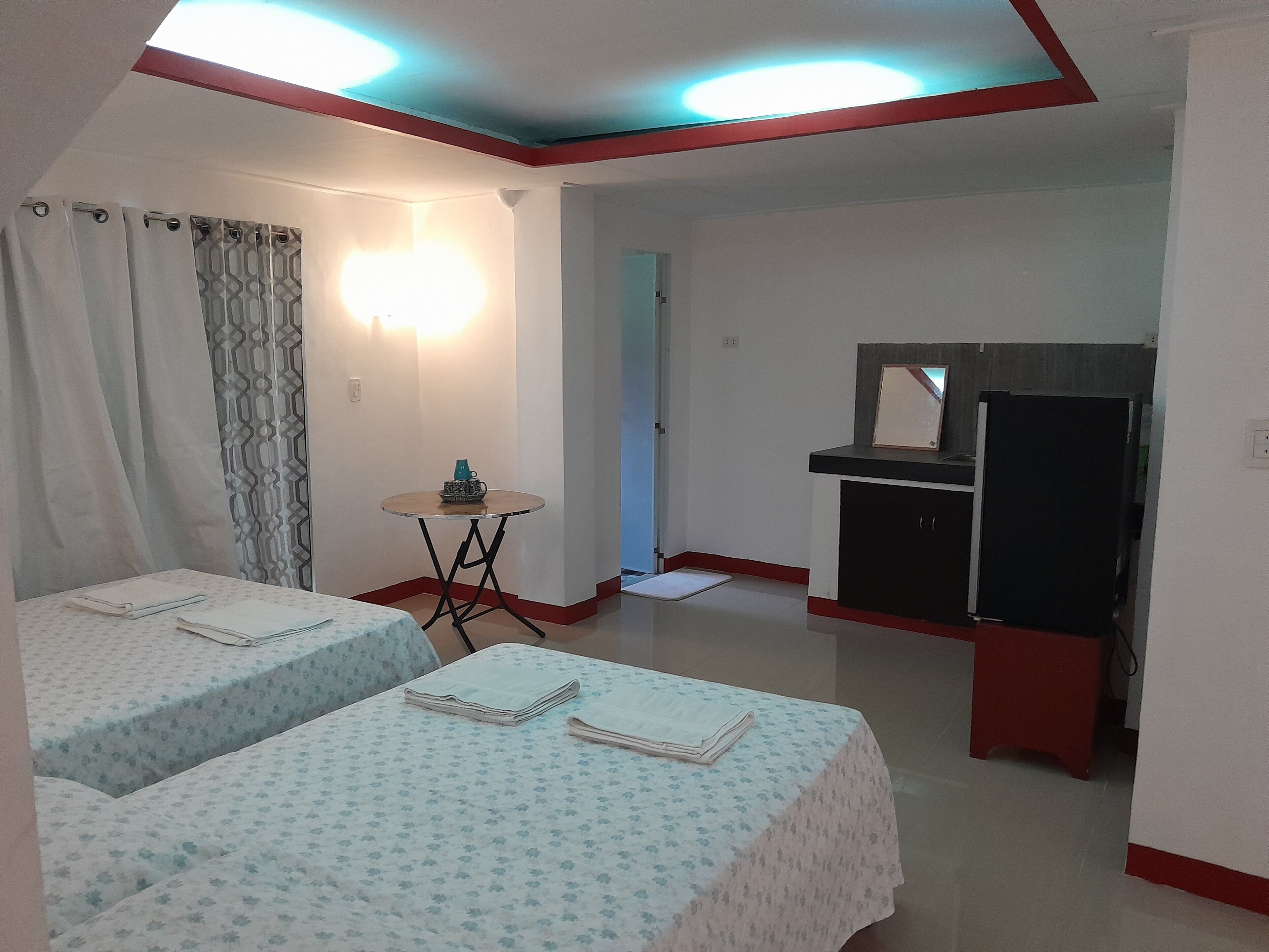 A hotel room with two beds, a small table, a TV, and a kitchenette.