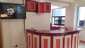 Un área de recepción con un mostrador rojo y blanco, un televisor montado en la pared y una pequeña mesa con cubierta de vidrio.