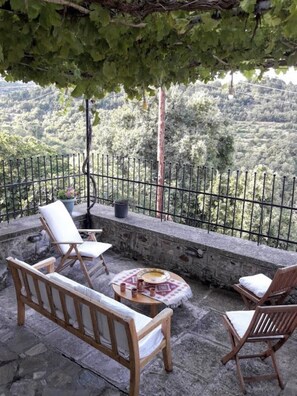Una terraza con muebles de madera, una mesa con mantel decorativo y vistas a un paisaje montañoso.