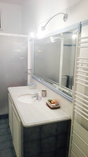 Ein Badezimmer mit einem großen Spiegel, einem Waschbecken und einer Dusche.