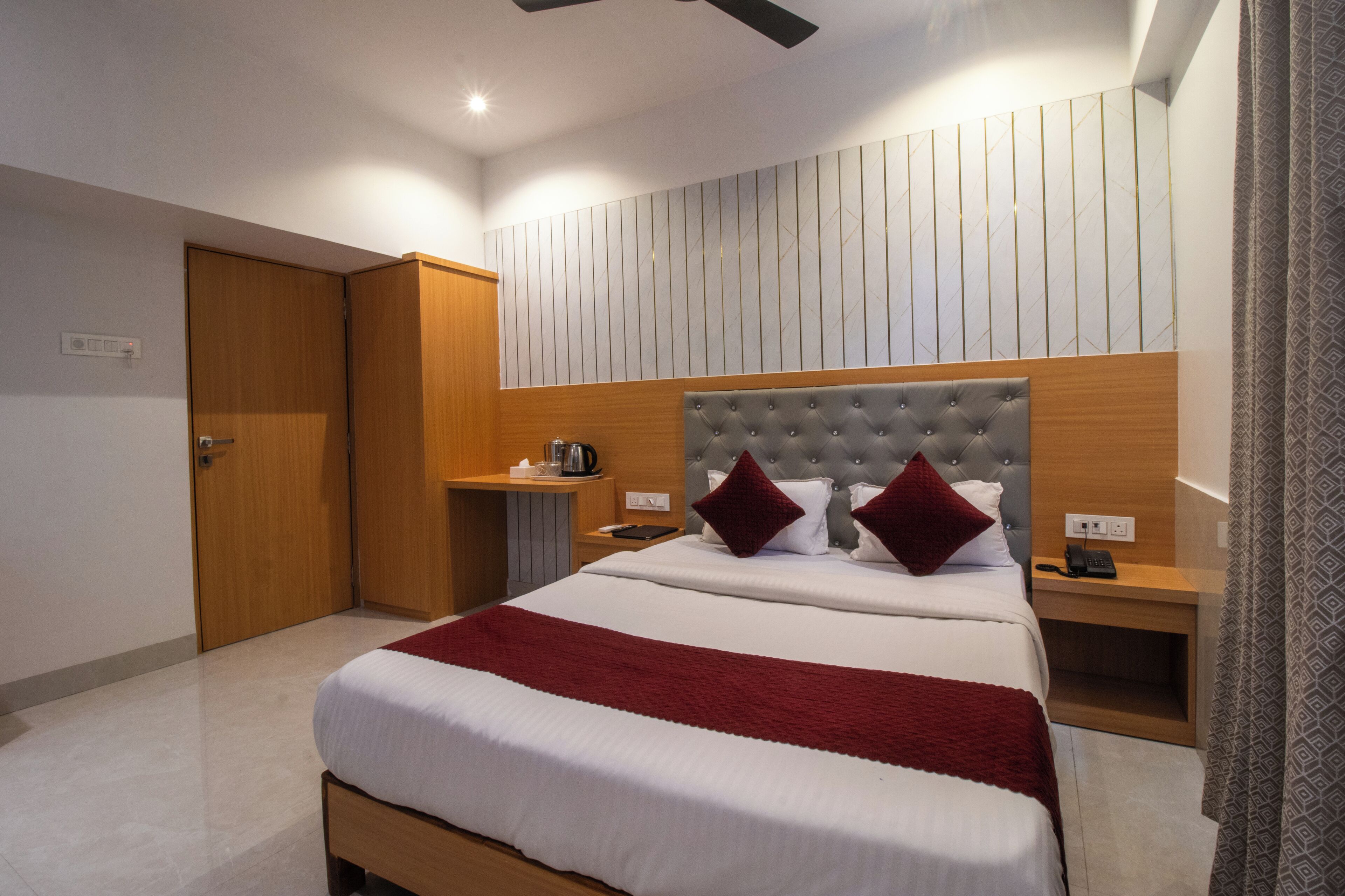 A hotel room with a large bed, a wooden headboard, a bedside table with a lamp, and a wardrobe.