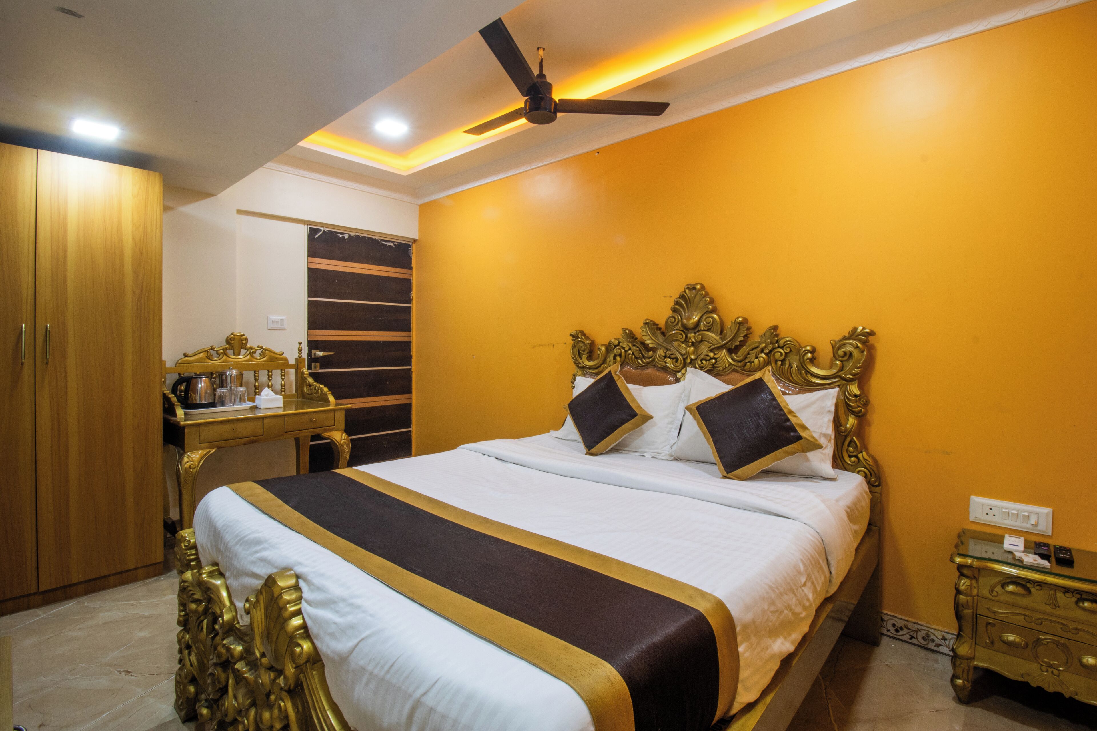A hotel room with a large bed, a ceiling fan, a wooden wardrobe, and a bedside table.