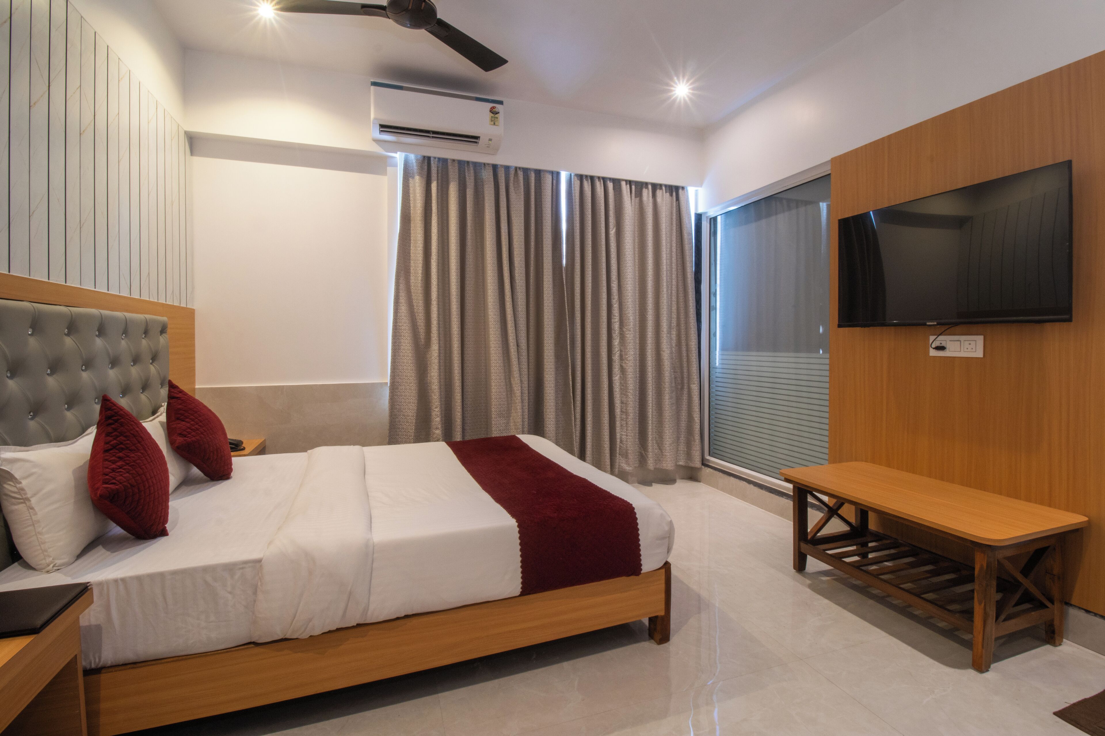 A modern bedroom with a bed, a TV, a bench, and an air conditioning unit.