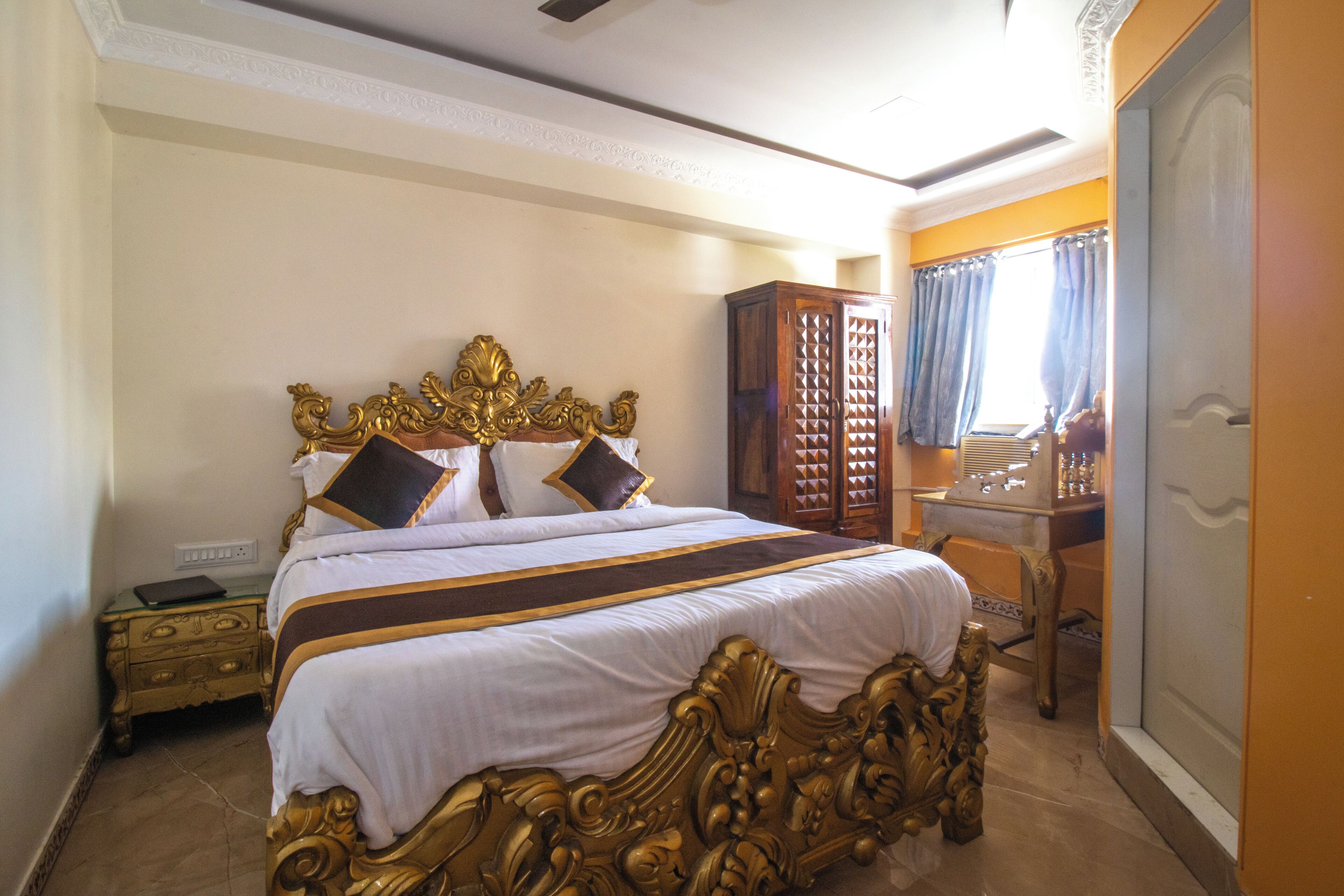 A large bed with ornate gold detailing, a wooden wardrobe, and a desk with a mirror.