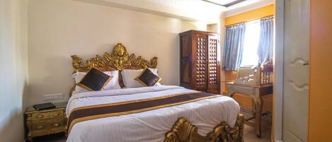A large bed with ornate gold detailing, a wooden wardrobe, and a desk with a mirror.
