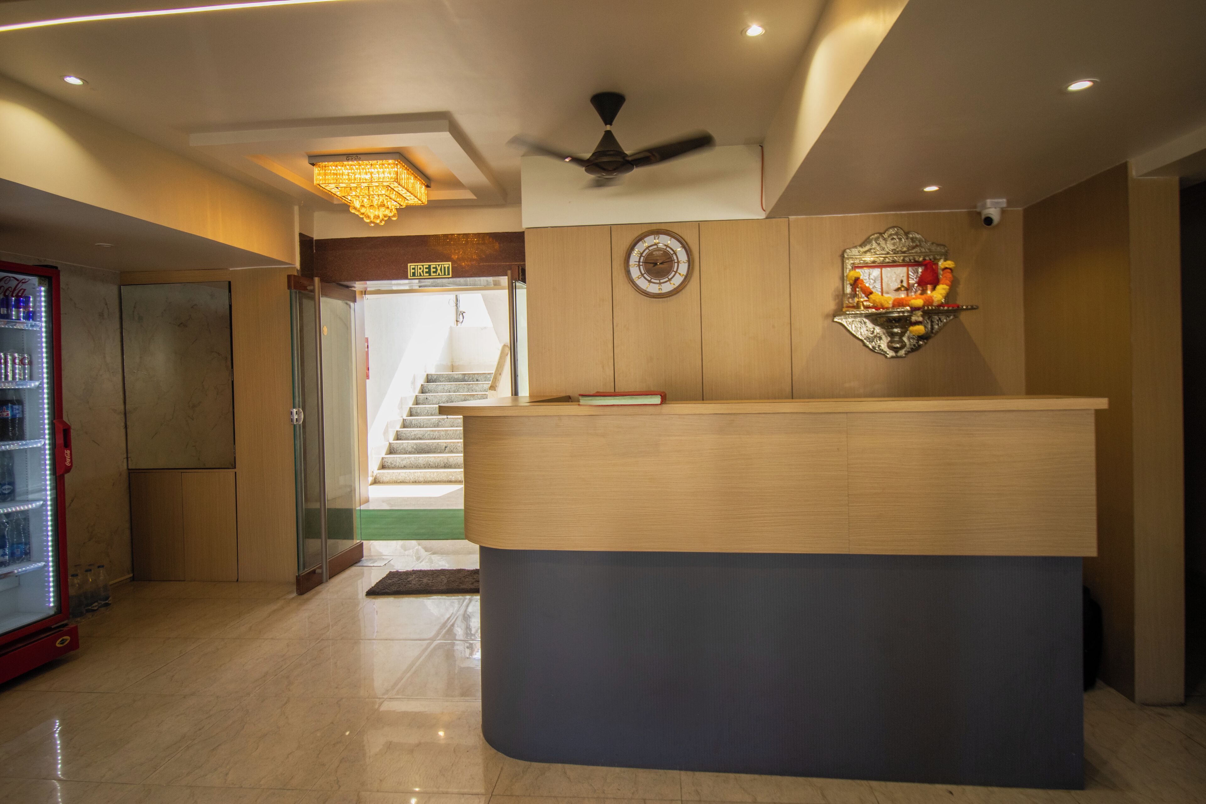 A hotel reception area with a wooden reception desk, a ceiling fan, a chandelier, and a staircase leading to the upper floors.