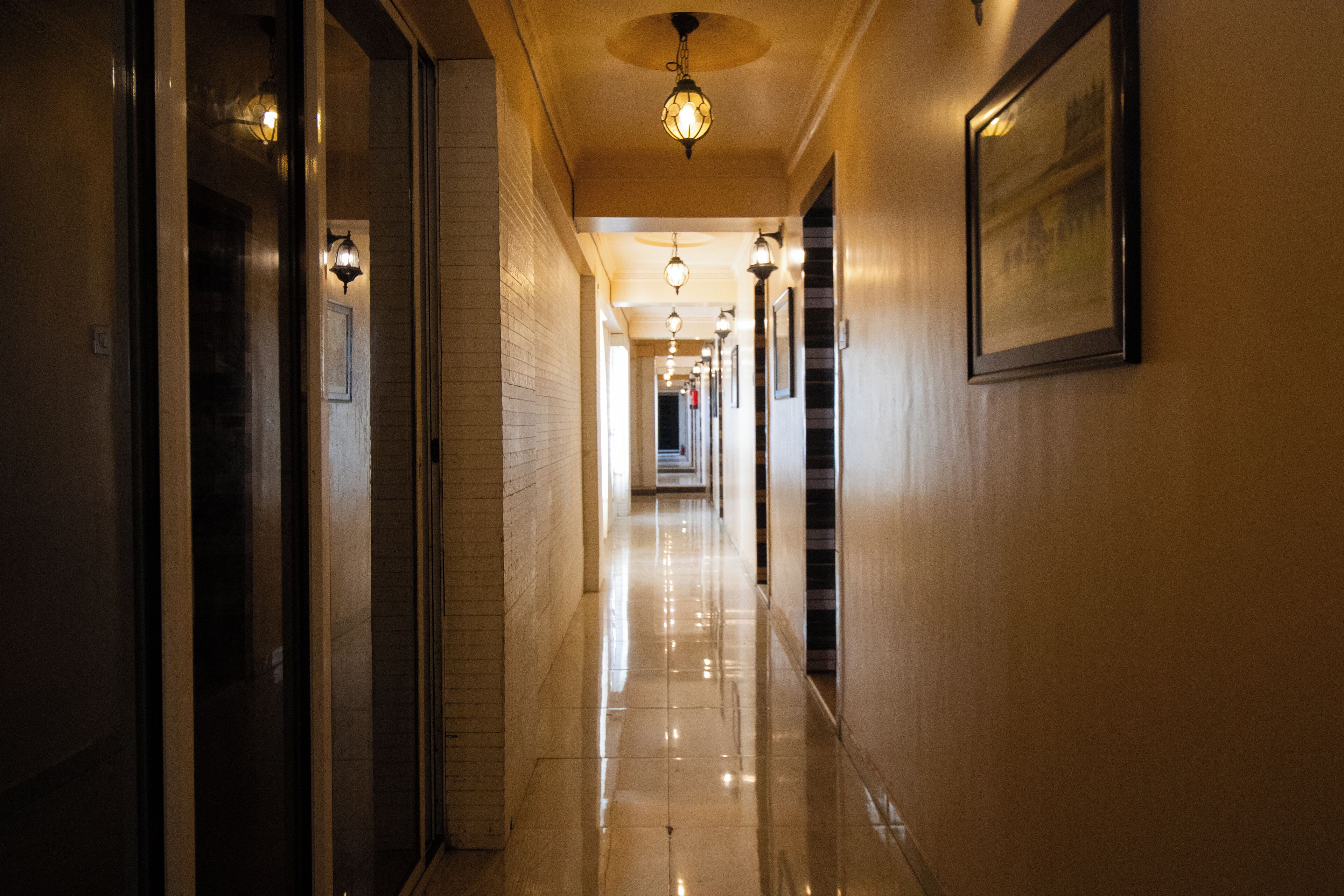 A hallway with a polished floor, wall-mounted lights, and framed pictures.