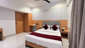 Une chambre d’hôtel moderne avec un grand lit, une table de chevet, une armoire, un ventilateur de plafond et un rideau à motifs.