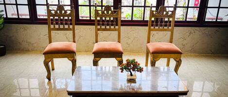 A room with a marble floor, a wooden table with a vase of flowers, and three wooden chairs with cushions.