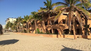 Un hôtel situé en bord de mer, avec des palmiers, une plage de sable fin et un ciel dégagé.