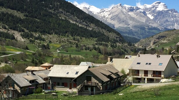 A rural village with traditional stone buildings, a small playground, and a view of snow-capped mountains. - Gîte "le Grand Ferrand" (Saint Etienne en Dévoluy)