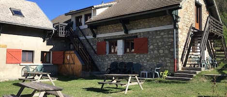 A rustic building with stone walls and wooden shutters, featuring outdoor seating and picnic tables.