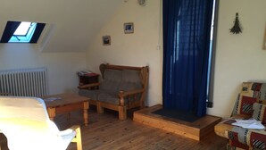 A cozy living room with a wooden floor, a sofa, a chair, a small table, and a window with a view. - Gîte "le Grand Ferrand" (Saint Etienne en Dévoluy)