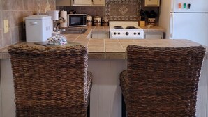 A kitchen with a central island, two wicker chairs, a microwave, a stove, and decorative wall-mounted cups.