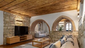 A living room with a stone wall, wooden ceiling, and arched windows. - Villa Simone - Luxury Villa with swimming pool (San Gimignano)
