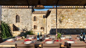 An outdoor dining area with stone walls and a pergola overhead. Tables are set with plates, glasses, and wine bottles. - Villa Simone - Luxury Villa with swimming pool (San Gimignano)