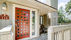Una casa de madera con puerta roja, un porche con banca y un letrero que dice "Beachwalk 114".