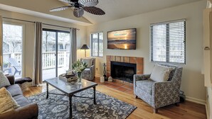 Un salón amplio con chimenea, ventilador de techo y un ventanal con persianas.