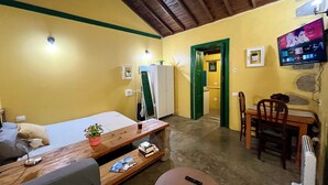 Habitación pequeña con cama, una mesita con una planta, televisor montado en la pared y puerta que da al baño.