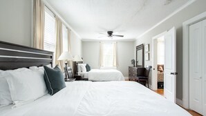 Un dormitorio con dos camas, un ventilador de techo, un aparador y una silla.