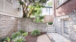Un muro de piedra con un pequeño jardín, una cerca de madera y una escalera que conduce a una puerta.
