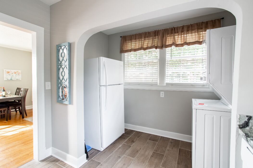 Una cocina con refrigerador, ventana con persianas y comedor con sillas y mesa.