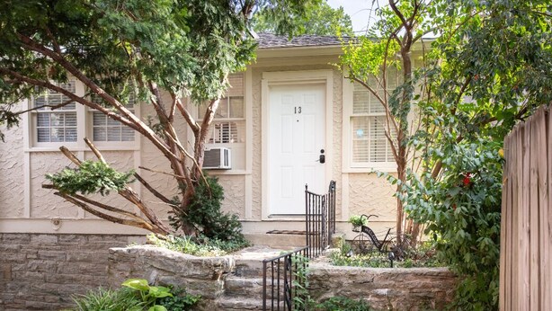 Una casa con una puerta blanca marcada con el número 13, una escalera de piedra que lleva al frente y una valla de madera.