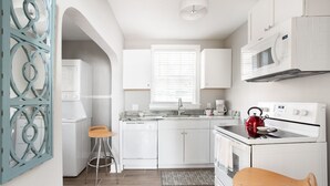 Una cocina compacta con gabinetes blancos, un microondas, una estufa y dos taburetes.
