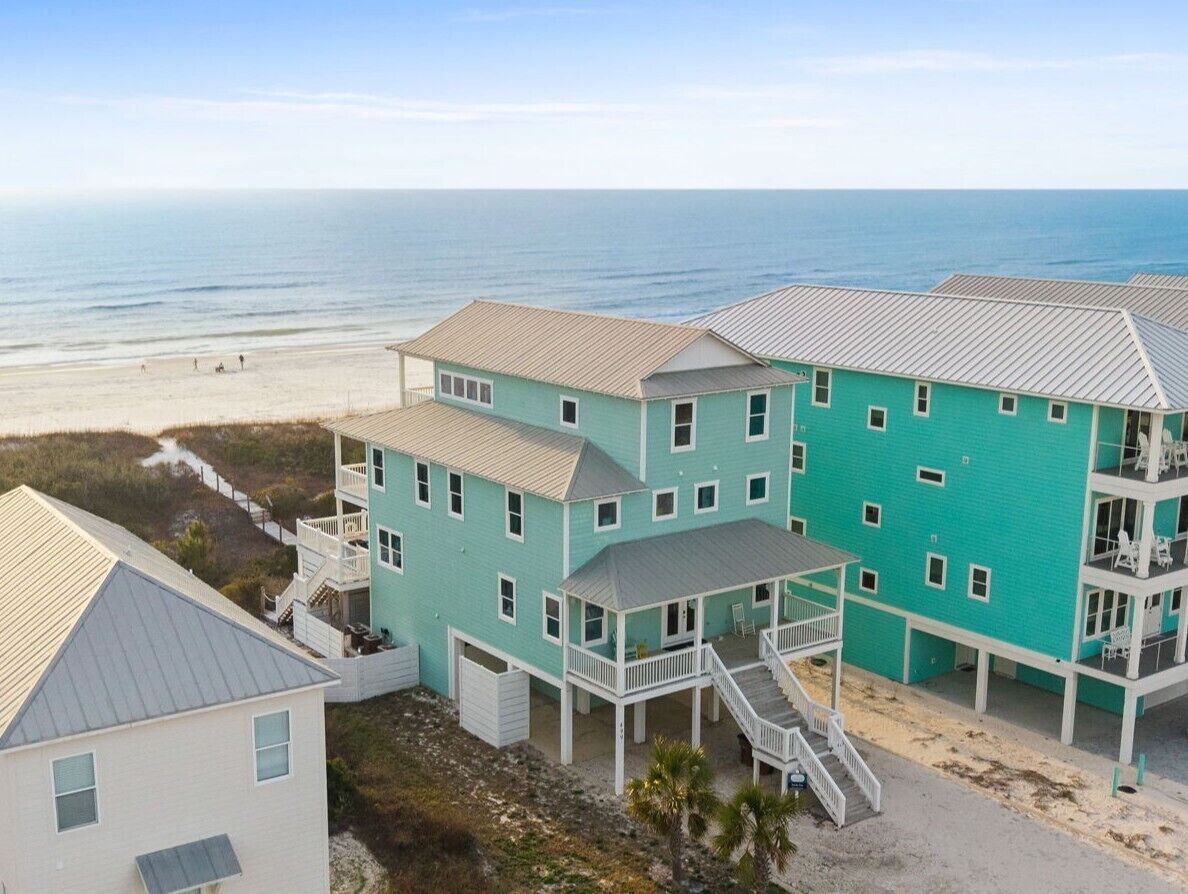A coastal property with multiple buildings, including a large turquoise house with a balcony and a smaller adjacent building.