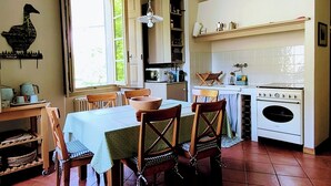 Une cuisine équipée d’une table à manger, de chaises, d’un luminaire suspendu, d’une cuisinière et d’une fenêtre.