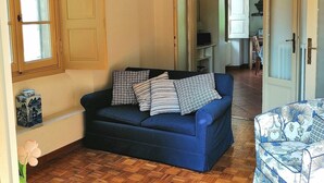 Un salon avec un canapé bleu, un pouf à motifs, un luminaire suspendu et un plancher en bois.