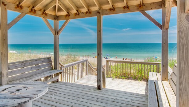 Una pérgola de madera en la playa con vista al océano.