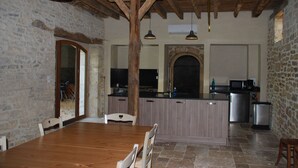 Une cuisine rustique aux murs en pierre, avec des poutres en bois et un îlot central doté d’un évier et d’un four à micro-ondes.
