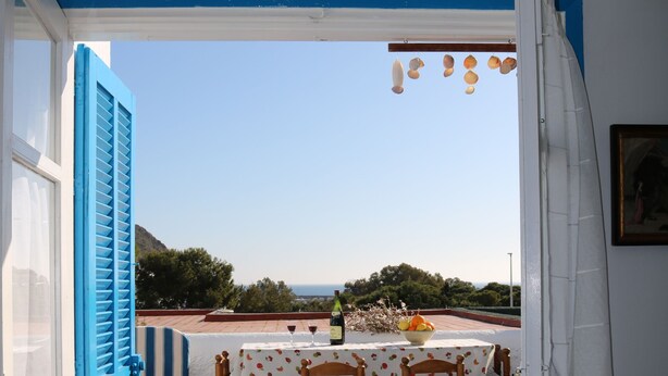 An open door leading to a patio with a table and chairs, a view of the sea, and a blue door with shutters. - Sea Foam - 5 people (San José)