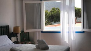 A hotel room with a bed, a window with curtains, a lamp, and a view of a mountainous landscape. - Sea Foam - 5 people (San José)