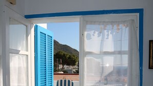 A room with a white door, a blue-framed window, and a view of a terrace with a chair and table. - Sea Foam - 5 people (San José)