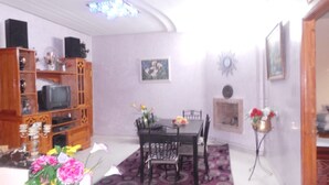 Un comedor con una mesa y sillas, un mueble de madera con un televisor, y un arreglo floral en el suelo.