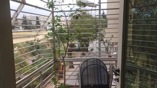 Un pequeño balcón con una silla, plantas en macetas y vista a la calle.