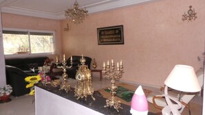 Un salón con sofá negro, una lámpara de araña, un reloj de pared y un adorno mural.