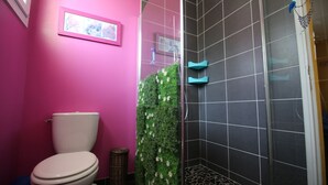 Ein Badezimmer mit einer rosa Wand, einer weißen Toilette, einer Dusche mit dunkel gefliesten Wänden und einer grünen Wand mit weißen Blumen.