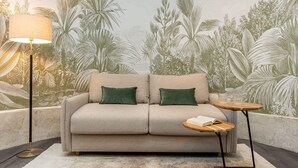 A sofa with two green cushions, a floor lamp, and a small wooden table with a book.