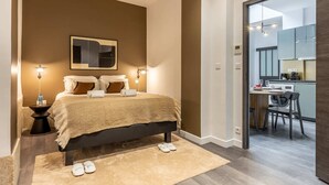 A modern bedroom with a large bed, bedside lamps, and a view into the kitchen area.