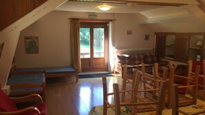 Ein gemütliches Dachzimmer mit schrägverlaufender Holzbalkendecke, einer Bank, einer Couch und einem Tisch mit Stühlen.