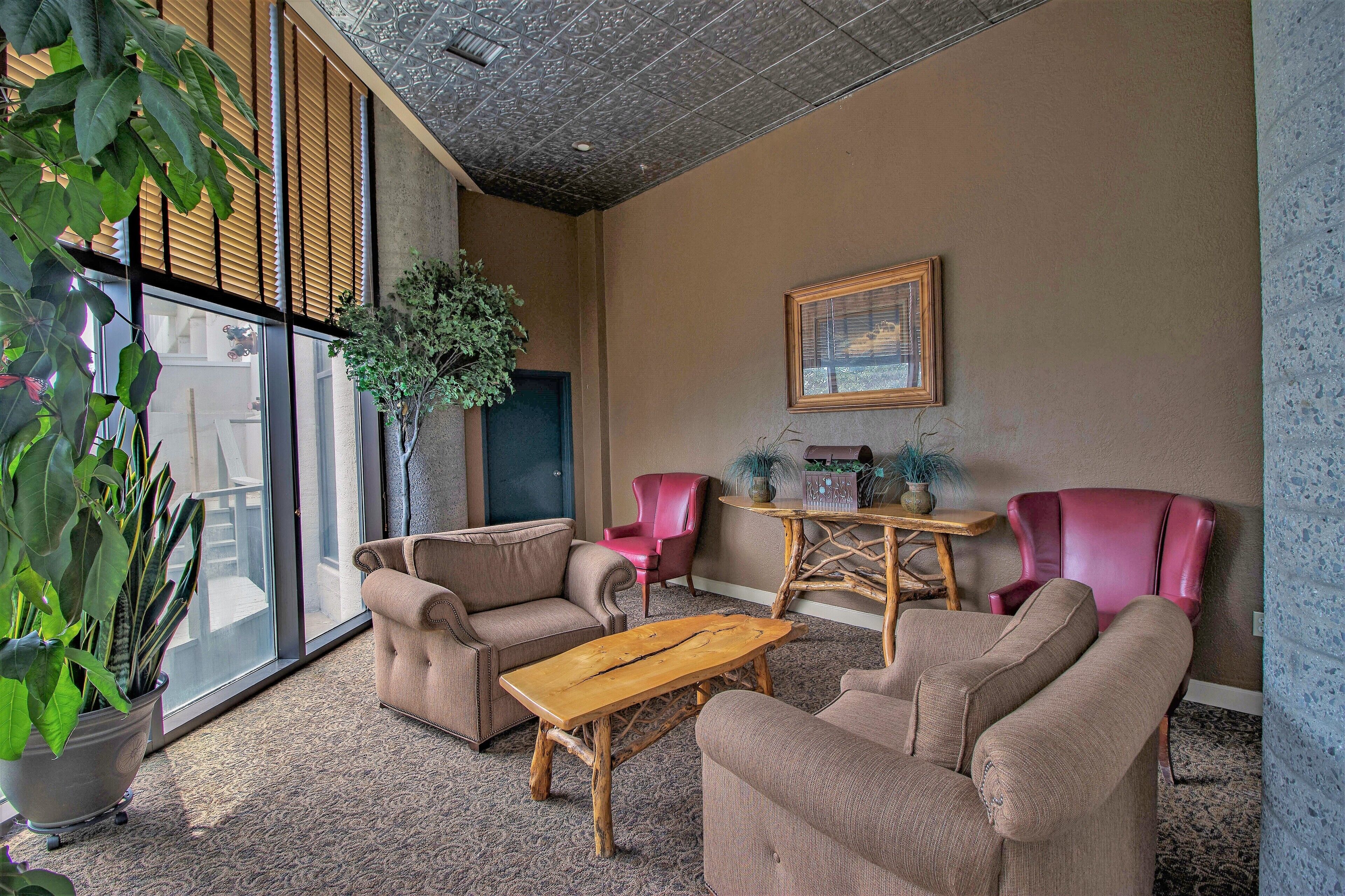 A spacious room with a large window, a wooden coffee table, beige sofas, and a pink chair.