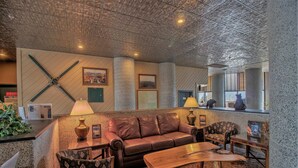 A lobby with a leather sofa, patterned chairs, a wooden coffee table, and a reception desk with a lamp. - Top Floor 2B Condo w/ Pool Access! (Sugar Mountain)