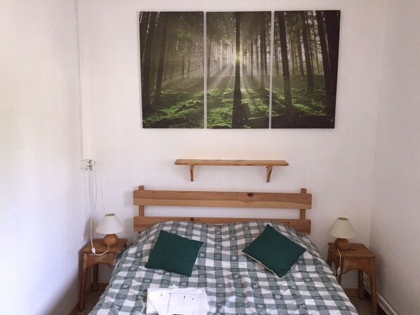 A bedroom with a checkered bedspread, two green pillows, a wooden headboard, a shelf above the bed, and two bedside lamps. - Gîte "the Pic Pierroux" (Saint Etienne en Dévoluy)
