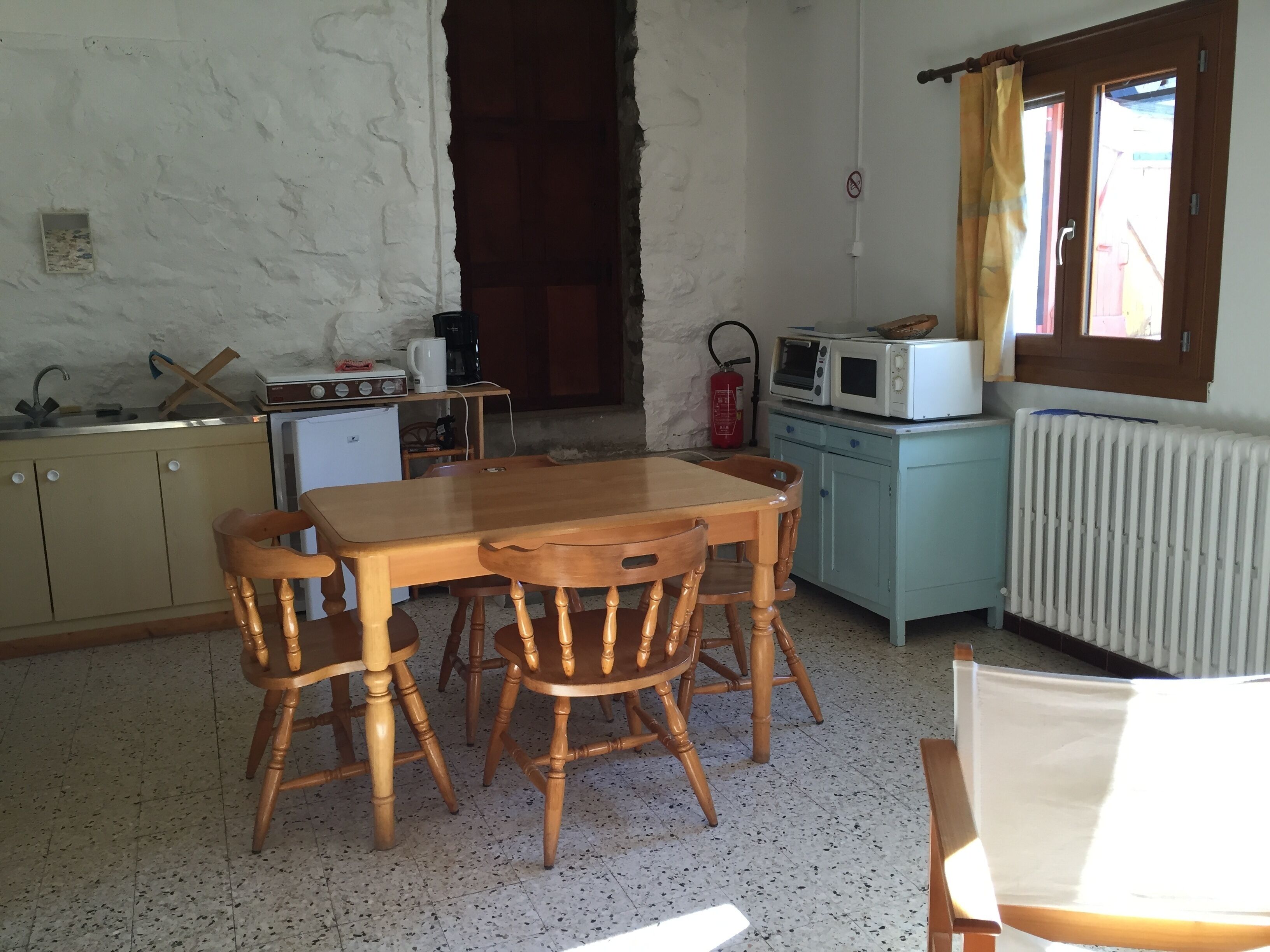 A compact kitchen with a wooden table and chairs, a small refrigerator, a microwave, and a radiator.