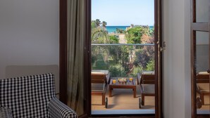 A room with a checkered sofa, a wooden floor, a balcony with a table and chairs, and a view of the sea. - Evdokia Beach Resort (Malevizi)